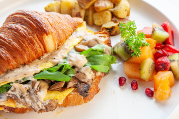 Mediterranean scrambled egg croissant sandwich with fruits and potatoes.