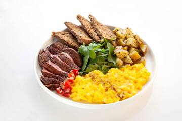 Tenderloin beef steak with scrambled eggs, rocket leaves and potatoes with a side of rye bread.