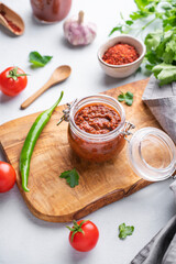 Homemade tomato sauce for pizza or pasta in a jar on a wooden board on a light background with fresh vegetables and herbs.