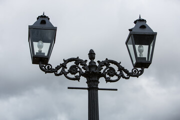 Fototapeta na wymiar Gothic black metal pole with two vintage style bulb lanterns in city