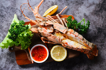 spiny lobster food on wooden cutting board, fresh lobster or rock lobster seafood with herb and spices lemon coriander parsley on dark, lobster for cooking food and seafood sauce - 580563579