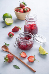 Homemade strawberry jam. Preserved food in a glass jar with fresh organic berries on a light background with lime.