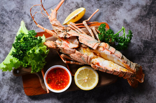 spiny lobster food on wooden cutting board, fresh lobster or rock lobster seafood with herb and spices lemon coriander parsley on dark, lobster for cooking food and seafood sauce