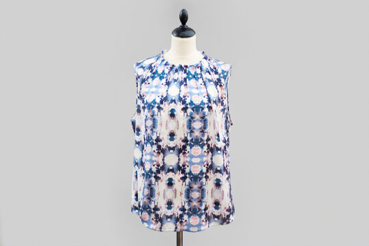 Blue and pink multicolored patterned floral short sleeve top blouse hangs on a yellow and white mannequin isolated by a gray backdrop.