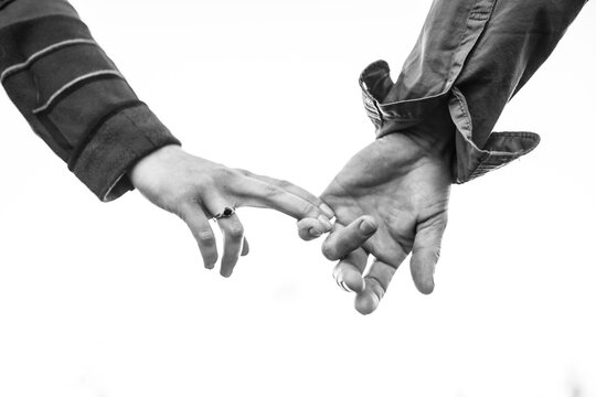 Woman hand holding to a mans hand barely with just a few fingers. Black and white concept photo