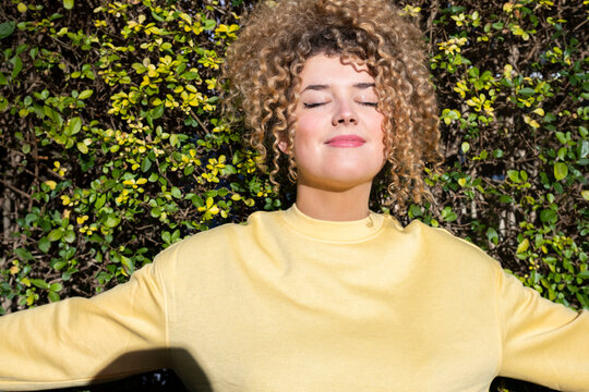 Smiling blond woman enjoying sunlight in front of plants