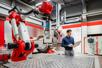 Engineer using laptop standing in robot factory