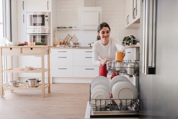 Woman arranging crockery in dishwasher at home