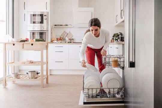 Woman arranging plates in dishwasher at home