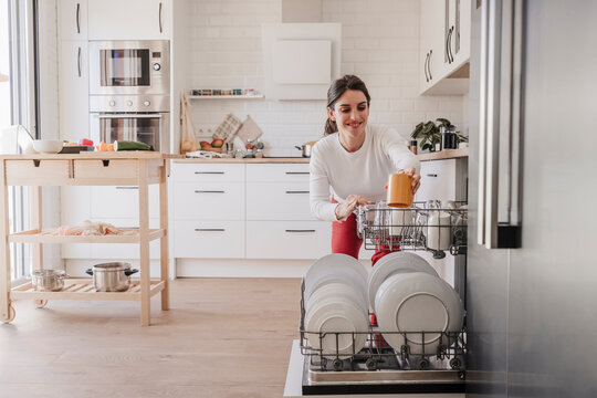 Woman arranging crockery in dishwasher at home