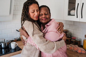 Woman with eyes closed embracing mother in kitchen at home