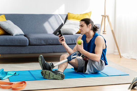 Young man with disability using smart phone sitting on exercise mat at home