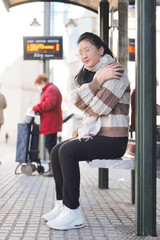 Young Asian girl with glasses sitting in the cold while waiting for the bus. Transportation concept.