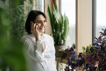 Smiling woman talking on smart phone by plants
