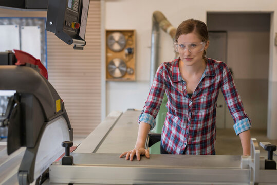 Smiling craftswoman leaning on wood cutting machine in workshop