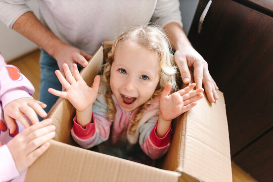 Happy girl sitting in cardboard box with sister and father at home