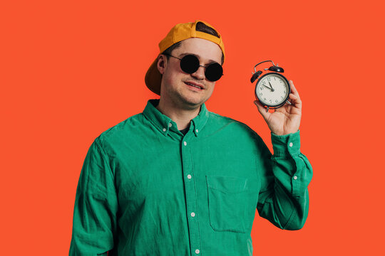 Happy man standing with alarm clock against coral background