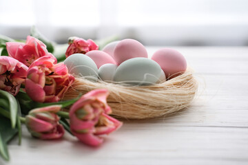 a nest with eggs in gentle pastel colors and a bouquet of tulips on a white background