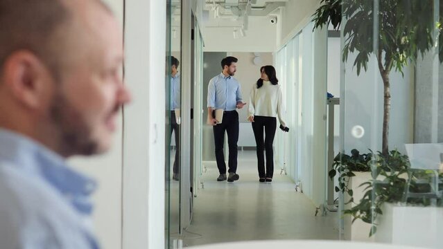 Busy man and woman walk through the office corridor and discuss business ideas. In the foreground, the man's face talks with female coworker. Emphasis on teamwork, office culture, motivational goals.