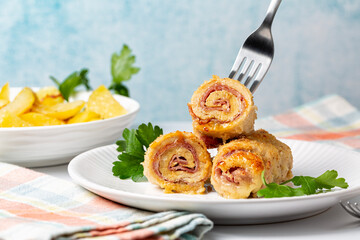 Eating chicken breast roll ups stuffed with cheese and ham, baked potato on a background. Light blue background.