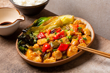 Sweet and sour chicken with bell peppers and sauce made of tomato, pineapple, soy sauce, vinegar. Sesame seeds and green onion. Bok choy, boiled rice. Asian cuisine, Chinese cuisine, Thai cuisine.