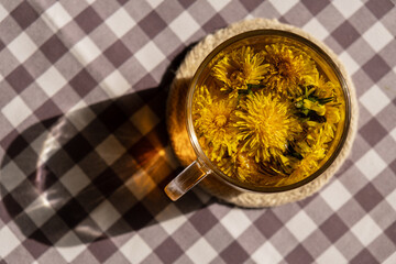 Dandelion flower healthy tea in glass cup on table. Herbal medicine Delicious tisane tea from with fresh yellow blossom dandelion flowers inside tea cup. Green clearing infusion Wildflowers 