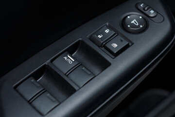 Obraz premium Arm rest with door lock buttons, window and mirror control panels. Close-up of a modern car door details, from inside view. Driver's seat