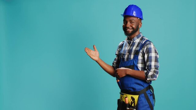African american repairman pointing at something in studio, indicating let or right direction for construction advertisement. Cheerful male carpenter presenting sideways for studio ad.