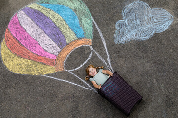 Happy little toddler girl flying in hot air balloon painted with colorful chalks in rainbow colors...