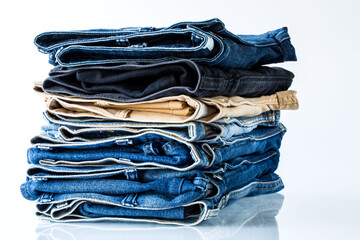 Close up stacked of blue, brown and black Jeans on white background.