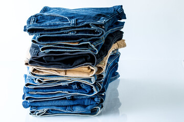 Close up stacked of blue, brown and black Jeans on white background.
