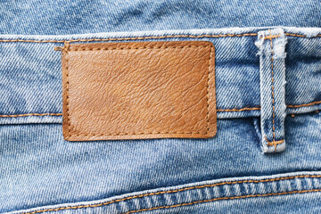 Fashion background with empty copy space for graphic design. Blank leather label tag. Blue jeans denim texture with thread sew lines. Brown clothing tag.