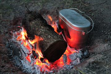 Atmospheric campfire in the forest with a burning log and a camping cauldron. Relaxation and tourism in the forest
