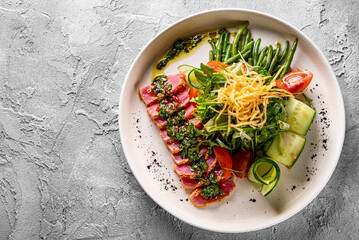 tuna slices with fresh vegetables and green beans salad on a plate.