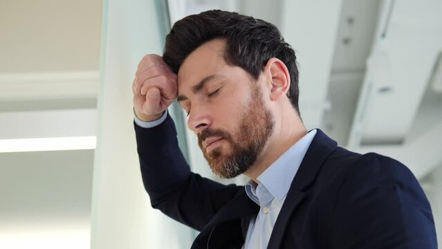 Work problems. A man businessman leans against the wall and holds his head, feeling strong migraine headaches due to financial problems, loss of a large sum, and unprofitable investments. Headache.