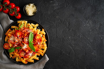 Fusilli pasta with tomatoes, basil, parmesan, and sauce on back background