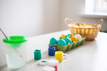 Ready-painted eggs stand on the table with paints and a wicker basket on a sunny day. Easter