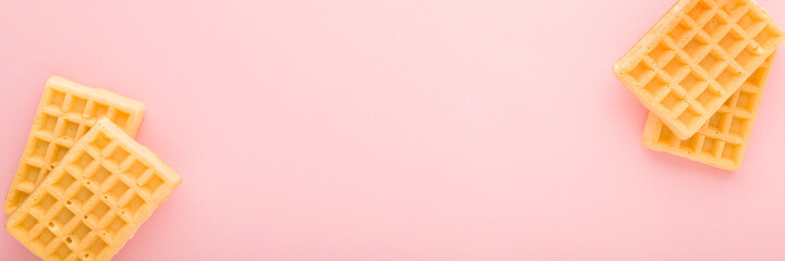 Fresh golden waffles on light pink table background. Pastel color. Wide banner. Closeup. Sweet snacks. Empty place for text. Top down view.