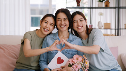 Enjoy good warm time Mother day two grown up kid child girl look at camera joy cuddle hug make heart shape love hand sign to mature mum. Asia middle age mom young adult three people smile happy face