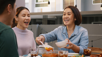 Mom enjoy thai meal cooking for family day home dining at dine table cozy patio. Mum passing serving food to group four asia people young adult man woman friend fun joy relax warm night picnic eating.