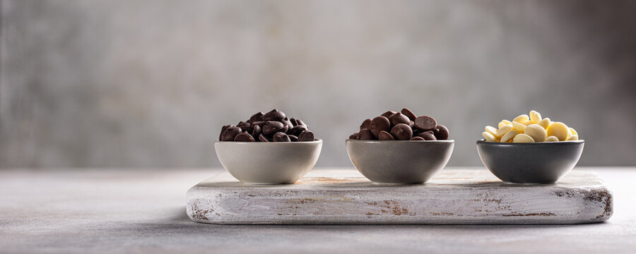 Banner with ingredients for cooking hot chocolate. White, milk and dark chocolate chips. Over gray background, copy space