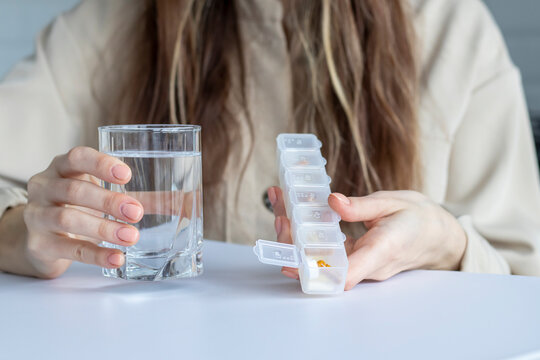 Woman is holding a Medication organizer with an open cell and is about to drink her daily dose of medication. Pill box, case, holder, container or caddy.