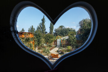Traditional rural hospitality, looking through a heart shaped window on a landscape with a village garden