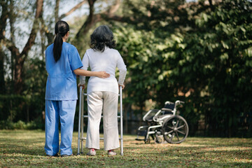 Asian careful caregiver or nurse and the happy patient in a wheelchair are walking in the garden to help and encourage and rest your mind with green nature. Help support yourself 