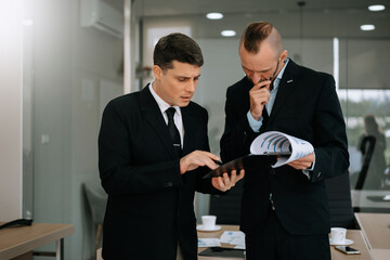 Male discussing new project with male colleague. Mature man talking with young man in office.