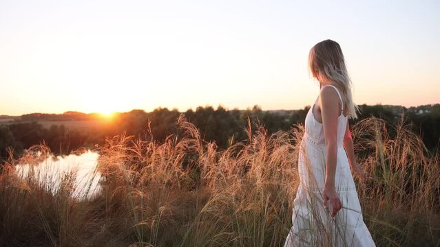 Young pretty woman in dress walks outdoors in field with amazing sunset. slow motion