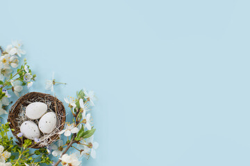 Stylish Easter eggs in nest and cherry blossoms flat lay on blue background with copy space. Happy Easter! Greeting card template. Modern holiday banner. Festive minimal composition