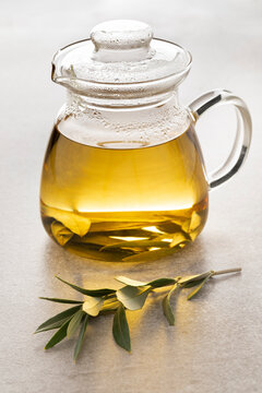 Glass tea pot with dried olive leaves tea and a fresh twig of olive leaves in front
