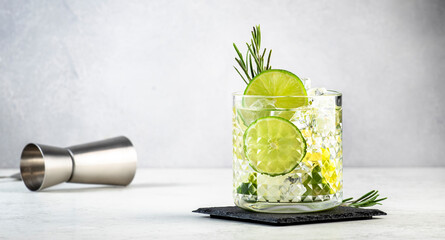 Gin tonic classic cocktail drink with dry gin, bitter tonic, lime and ice. Gray table background