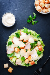 Caesar salad with chicken, iceberg salad, croutons, parmesan cheese with caesar dressing. Traditional recipe. Black table background, top view